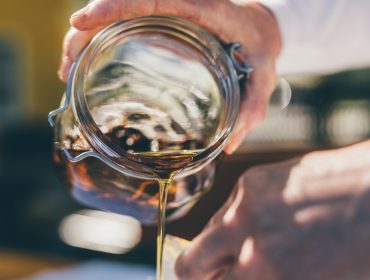 Jemand lässt Honig aus einem Glas tropfen