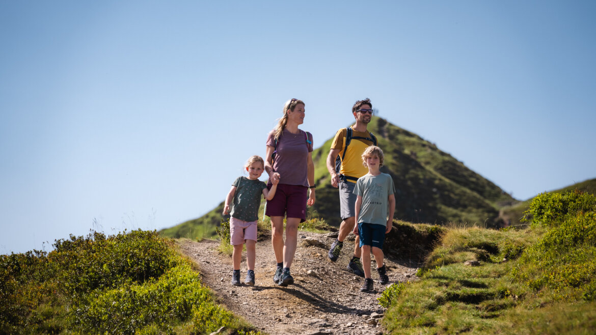 Eine vierköpfige Familie wandert an einem sonnigen Tag auf einem Bergweg in Saalbach Hinterglemm im Grünen. (vergrößerte Ansicht)