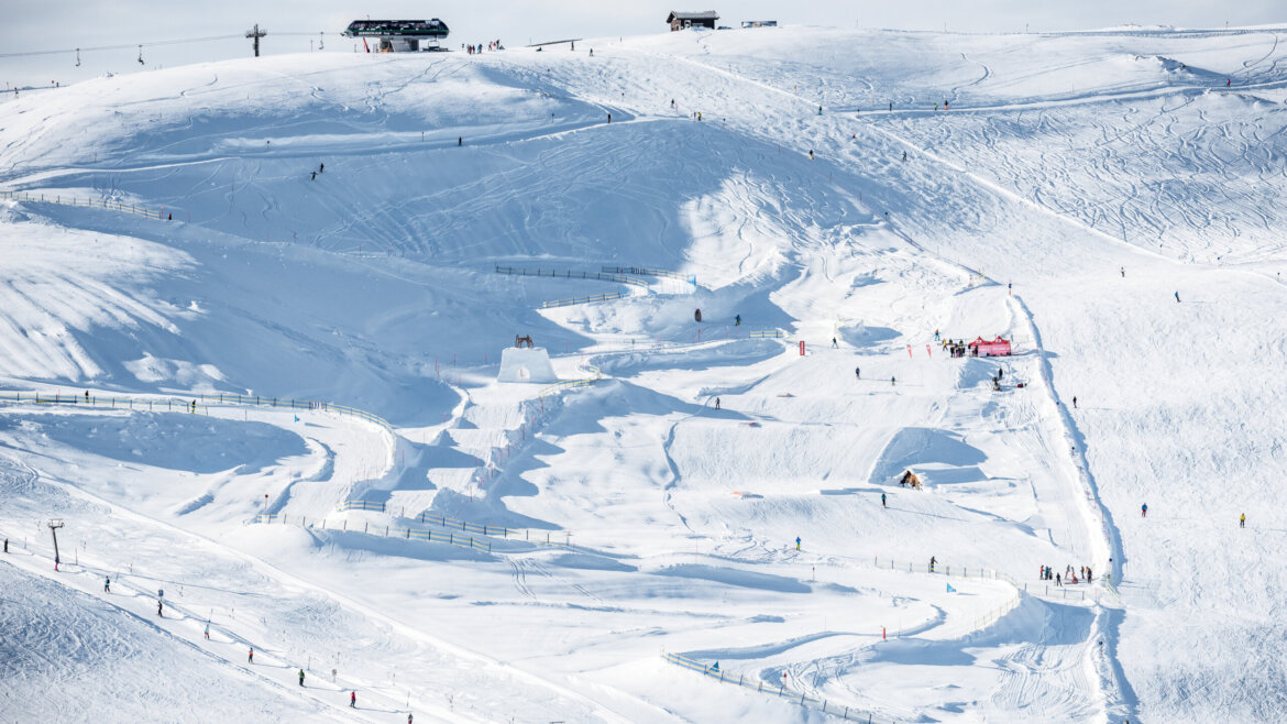 Schneebedeckte Skipisten in Neukirchen mit Pisten, Skifahrern und Skiliften an einem sonnigen Wintertag. (vergrößerte Ansicht)