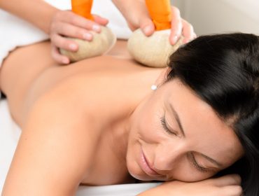 Eine Frau genießt Wellnessanwendungen mit einer wohltuenden Kräuterkompressenmassage in einer ruhigen Spa-Umgebung.