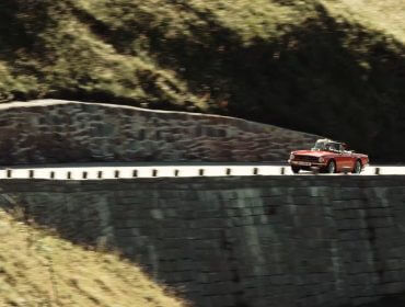 Ein rotes Cabrio kreuzt die Panoramastraßen und schlängelt sich zwischen Steinmauern und grasbewachsenen Berghängen hindurch.