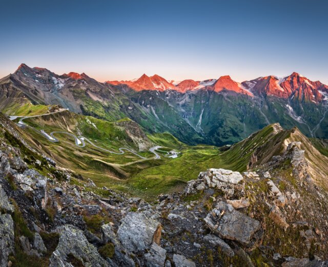 Kurvenreiche Bergstraße durch grünes Tal in der Ferienregion Nationalpark Hohe Tauern bei Sonnenaufgang.