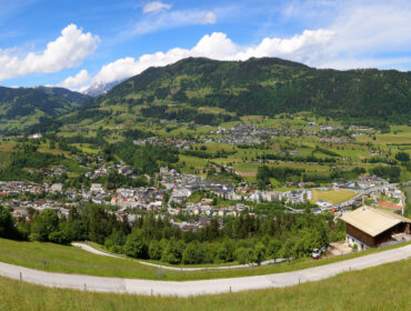 Panoramablick auf Schwarzach, eingebettet in ein grünes Tal mit verstreuten Häusern unter einem teilweise bewölkten Himmel.