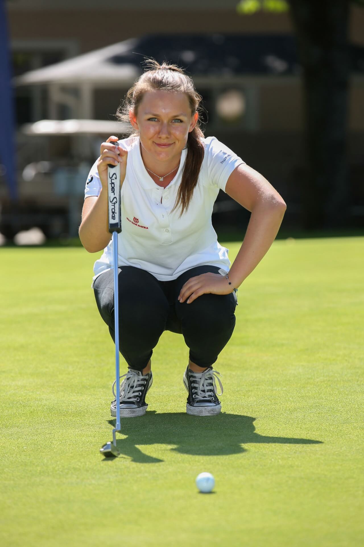 Junge Golferin hockt am Putting Green und denkt über ihren Putt nach