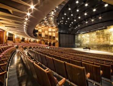 hires-grosses_festspielhaus_2_c_sf_andreas_kolarik (1) Leeres Theater mit hölzernen Sitzreihen vor einer Bühne, auf der die Salzburger Osterfestspiele am Klavier stattfinden.