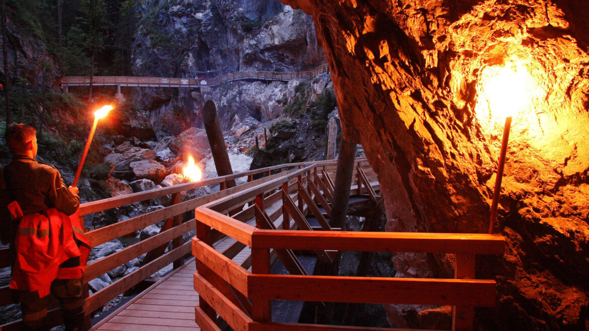 Kitzlochklamm © TVB Taxenbach Eine Person geht mit einer Fackel über einen Holzweg in der feuerbeleuchteten Felsenschlucht der Ferienregion Nationalpark Hohe Tauern. (vergrößerte Ansicht)