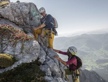 Zwei Kletterer mit Helmen und Seilen besteigen einen felsigen Berg in der Nähe des malerischen Saalfeldener Tals.