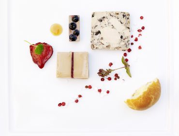 Ein Gourmetteller der Kulinarischen Leitbetriebe mit verschiedenen Käsesorten, Beeren, rosa Pfefferkörnern und frischen Kräutern.