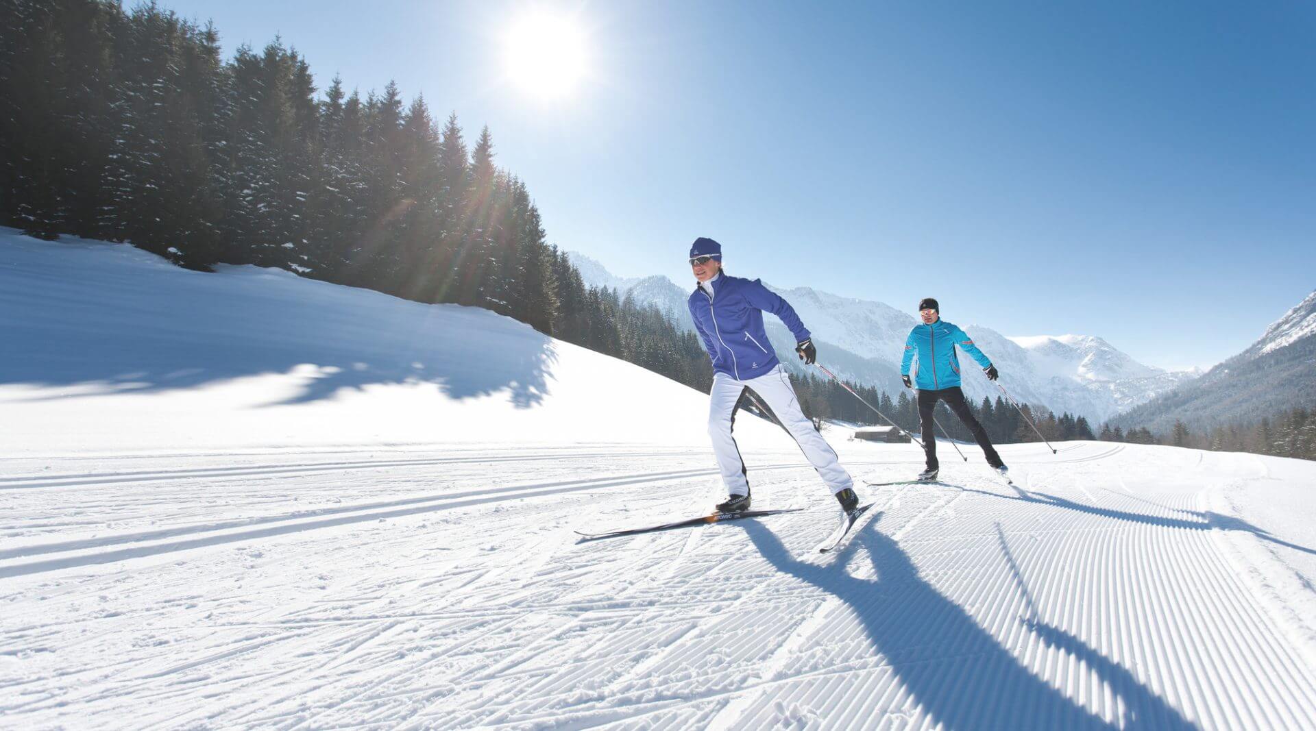 Dwóch narciarzy na biegówkach w promieniach zimowego słońca, na trasie do biegów stylem dowolnym.