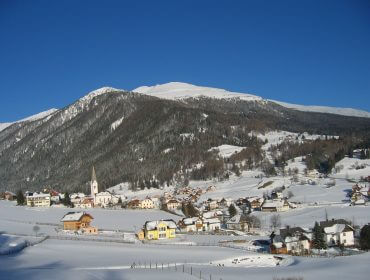 Das Dorf Lessach im Lungau unter einer Schneedecke, Häuser, eine Kirche, ein Berg