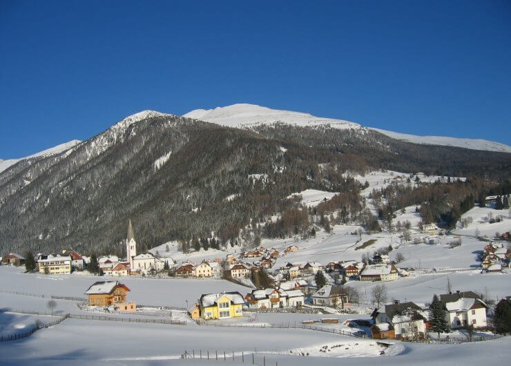 Das Dorf Lessach im Lungau unter einer Schneedecke, Häuser, eine Kirche, ein Berg