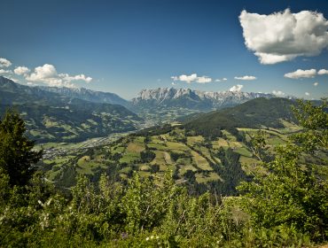 Ein Panoramablick auf grüne Täler und Hügel in der Nähe von St. Johann in Salzburg unter einem blauen Himmel mit vereinzelten Wolken.