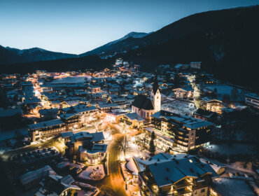 Neukirchen in der Abenddämmerung. Das verschneite Dorf und die beleuchtete Kirche bilden eine bezaubernde Winterlandschaft.