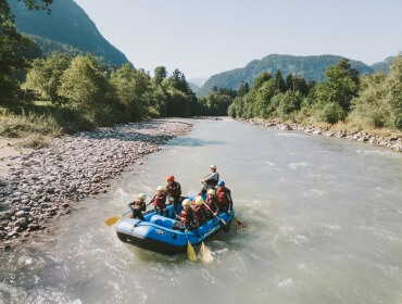 Eine Gruppe von Raftingfahrern auf dem Saalachtal, umgeben von Bäumen und Bergen, an einem sonnigen Tag.