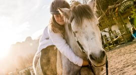 Ein Mädchen sitzt auf einem weiß-grauen Pferd und schlingt die Arme um dessen Hals.