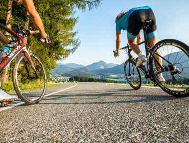 Zwei Radfahrer liefern sich auf einer einsamen Straße ein Renen entlang eines Sees.