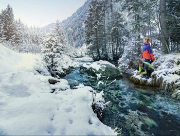 Zwei Läufer erfrischen sich am glasklaren Bach in einem verschneiten Wald