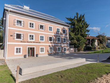 Ein pfirsichfarbenes, dreistöckiges Gebäude in Oberndorf mit der Aufschrift Stille Nacht Museum unter strahlend blauem Himmel.