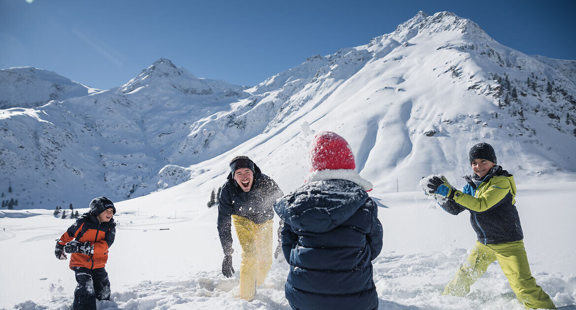 Vier Personen in Winterkleidung vergnügen sich bei einer Schneeballschlacht im verschneiten Talboden von Sportgastein unter strahlend blauem Himmel. (vergrößerte Ansicht)