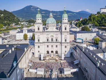 Salzburger Festspiele, Jedermann Domplatz Salzburg, Tobias Moretti Luftaufnahme einer großen Kathedrale mit grünen Zwillingskuppeln, Bergen und den Salzburger Festspielen vor der Tür.