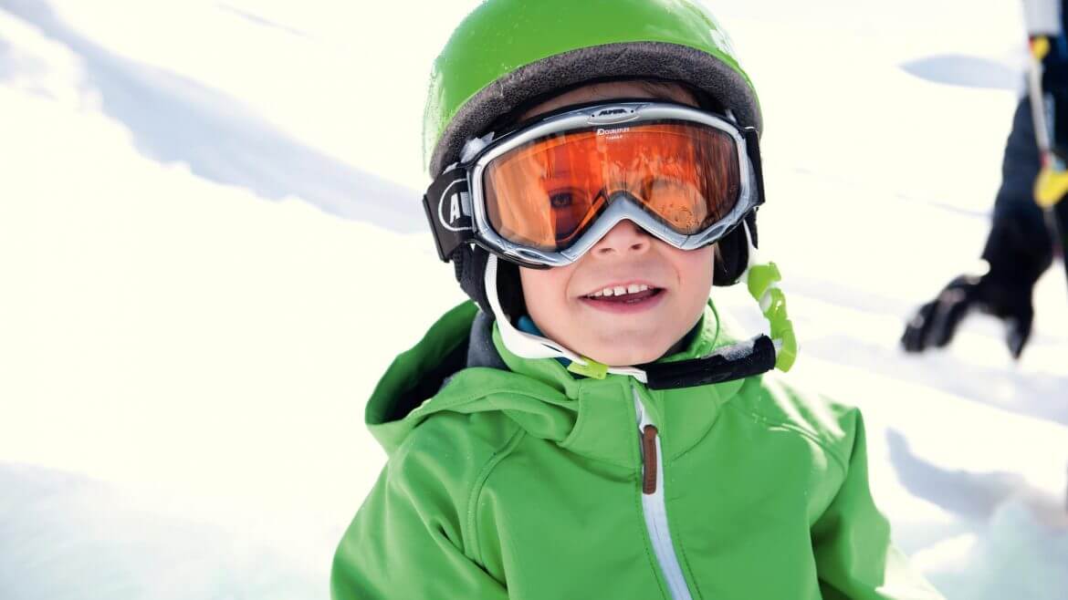Bub mit grüner Jacke und grünem Helm hat sichtlich Spaß im Schnee