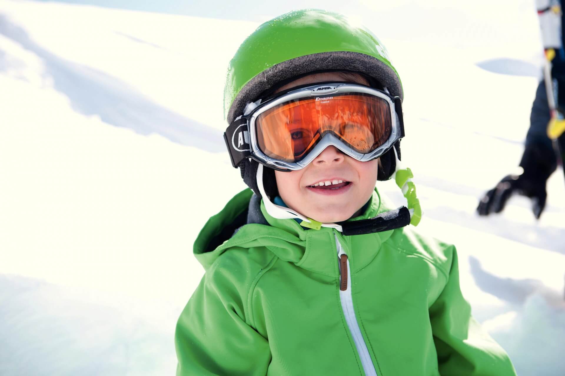Bub mit grüner Jacke und grünem Helm hat sichtlich Spaß am Skifahren