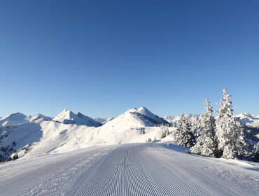 Eine schneebedeckte, präparierte Skipiste im Großarltal führt unter einem strahlend blauen Himmel zu fernen Bergen.