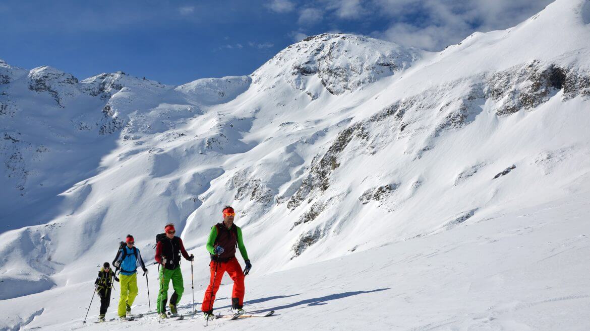 Vier Skitourengeher steigen langsam dem Gipfel entgegen.