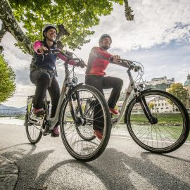 Zwei Radfahrer fahren am Ufer der Salzach auf dem Tauernradweg durch die Stadt Salzburg.