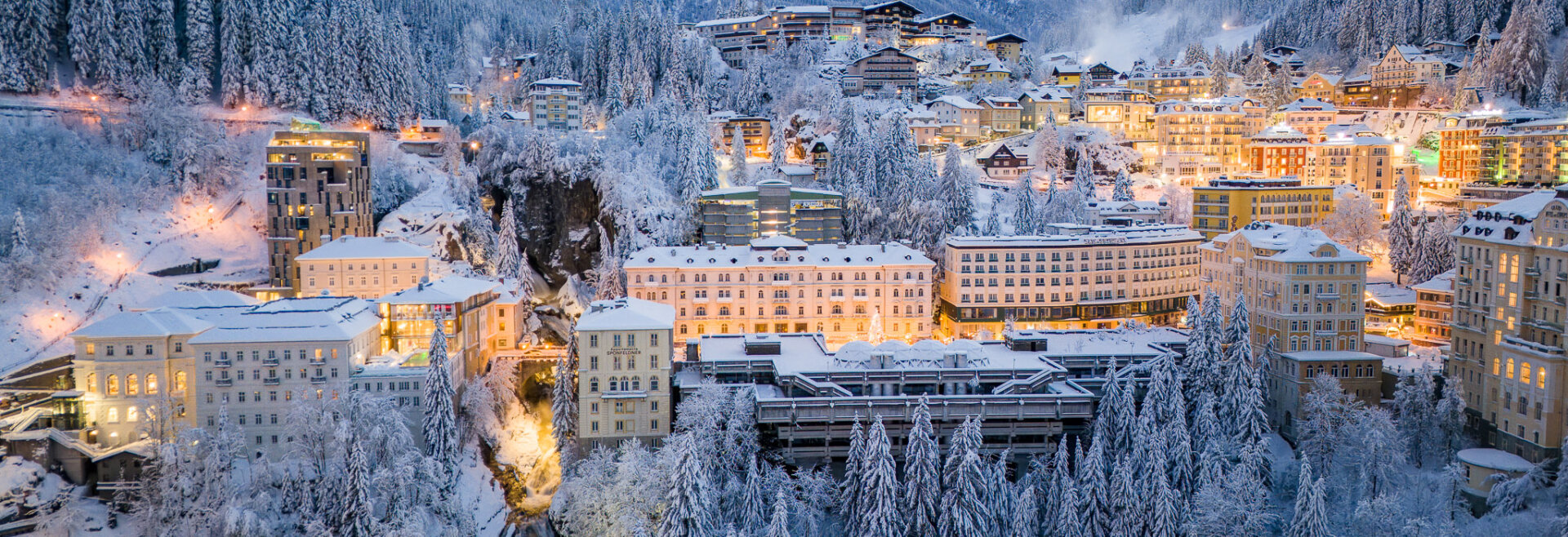 Das verschneite Bad Gastein, eingebettet in ein Bergtal, mit beleuchteten Gebäuden und Tannenbäumen ringsum.