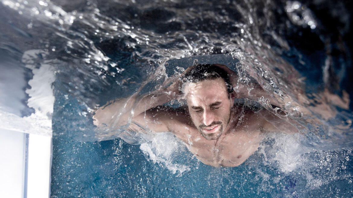 Ein Mann schwimmt im Gasteinertal unter Wasser, die Augen geschlossen, die Hände am Kopf, während das Wasser um ihn herum plätschert. (vergrößerte Ansicht)