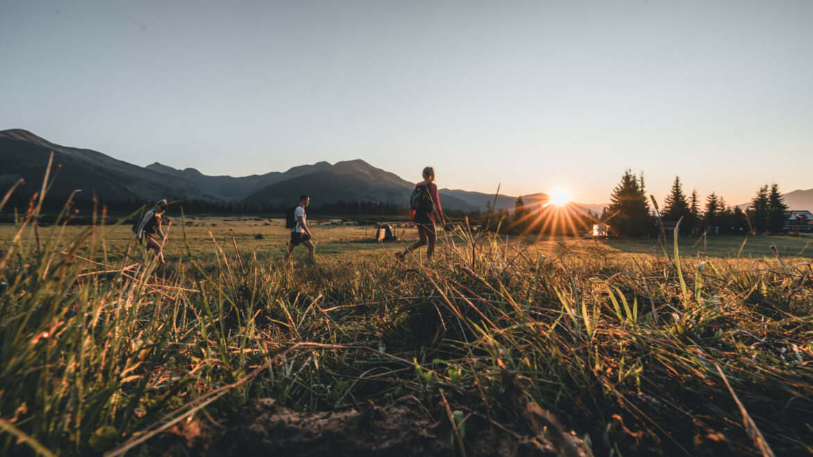 Wildgerlostal NPHT (c)Ferienregion Nationalpark Hohe Tauern_Daniel Kogler Vier Personen gehen bei Sonnenuntergang durch eine Wiese in der Ferienregion Nationalpark Hohe Tauern. (vergrößerte Ansicht)