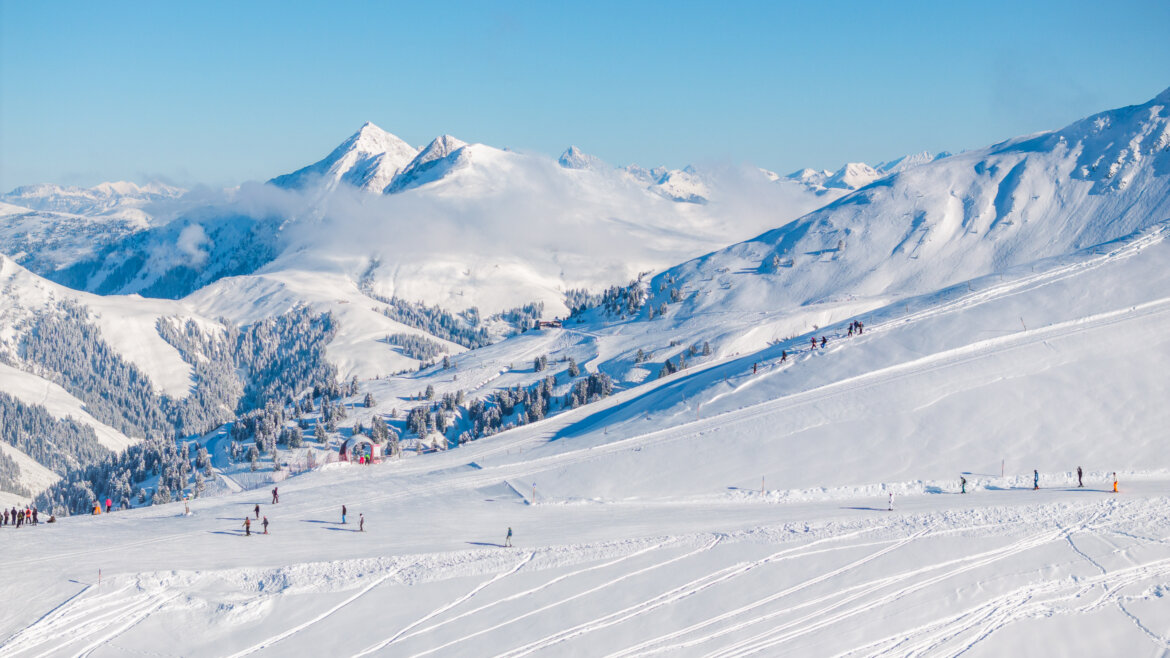 Schneebedeckte Neukirchener Berge mit Skifahrern und Snowboardern auf den Pisten unter einem klaren blauen Himmel. (vergrößerte Ansicht)