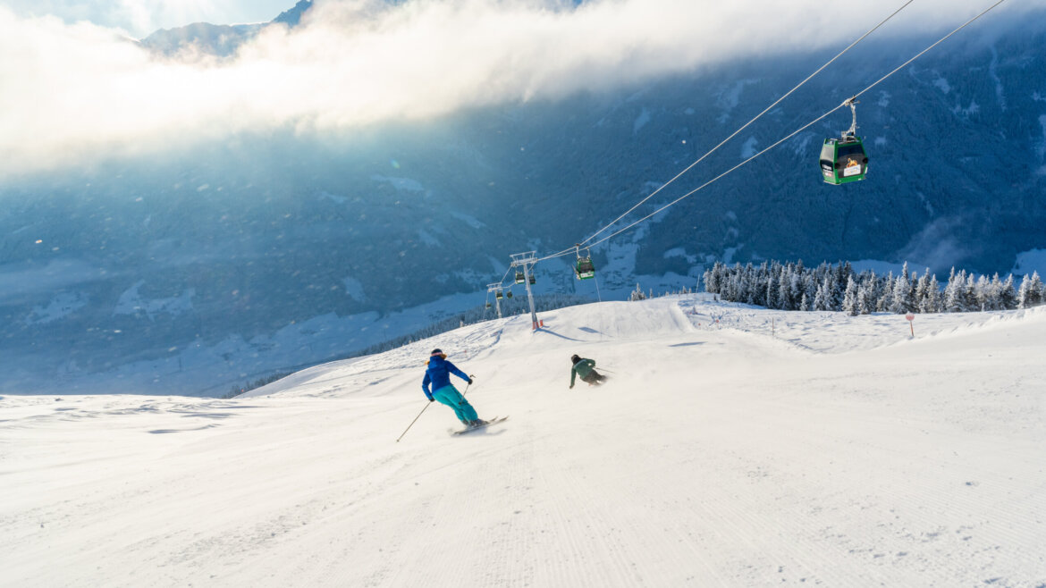 Zwei Personen beim Skifahren in Bramberg, verschneite Pisten und Skilifte vor der Kulisse der Berge. (vergrößerte Ansicht)