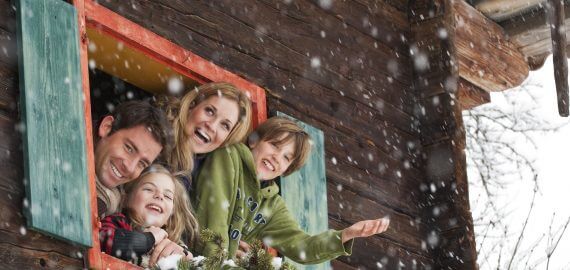 Familie beugt sich aus dem geöffneten Bauernhoffenster und freut sich über die Schneeflocken