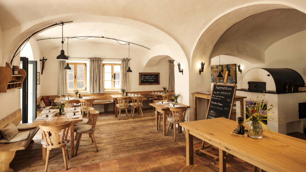 Gemütliches, rustikales Restaurant mit Holztischen, Gewölbedecken und Stiegl-Bier, das mit Blumen auf jedem Tisch serviert wird.
