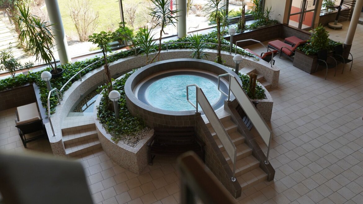 (c) Aqua Salza Runder Innenwhirlpool im Aqua Salza, umgeben von Pflanzen, Treppen und Liegestühlen an großen Fenstern. (vergrößerte Ansicht)