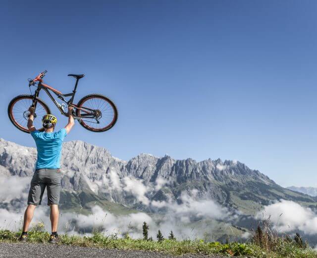 hochkönig-sommer-biken Biker stemmt vor der Kulisse des Hochkönigs sein Bike hoch.