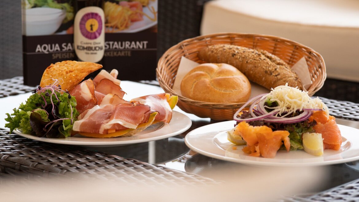 (c) Aqua Salza Ein Tisch mit Wurstwaren, geräuchertem Lachssalat, Brötchen und der Speisekarte des Aqua Salza im Hintergrund. (vergrößerte Ansicht)