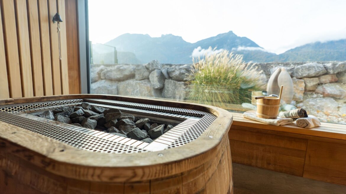 (c) Aqua Salza Holzsauna im Aqua Salza mit heißen Steinen, Blick auf die Berge und einem Eimer und einer Kelle auf der Bank. (vergrößerte Ansicht)