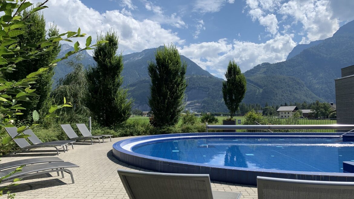 (c) Aqua Salza Außenpool des Aqua Salza mit Liegestühlen, umgeben von Bäumen und Bergen unter einem bewölkten Himmel. (vergrößerte Ansicht)