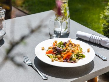 Ein frischer Gemüsesalat auf einem weißen Teller, geeignet für Unverträglichkeiten oder Allergene, draußen im Sonnenlicht anrichten.