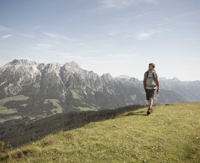Mann beim Wandern über eine Almwiese, im Hintergrund schroffe Berge