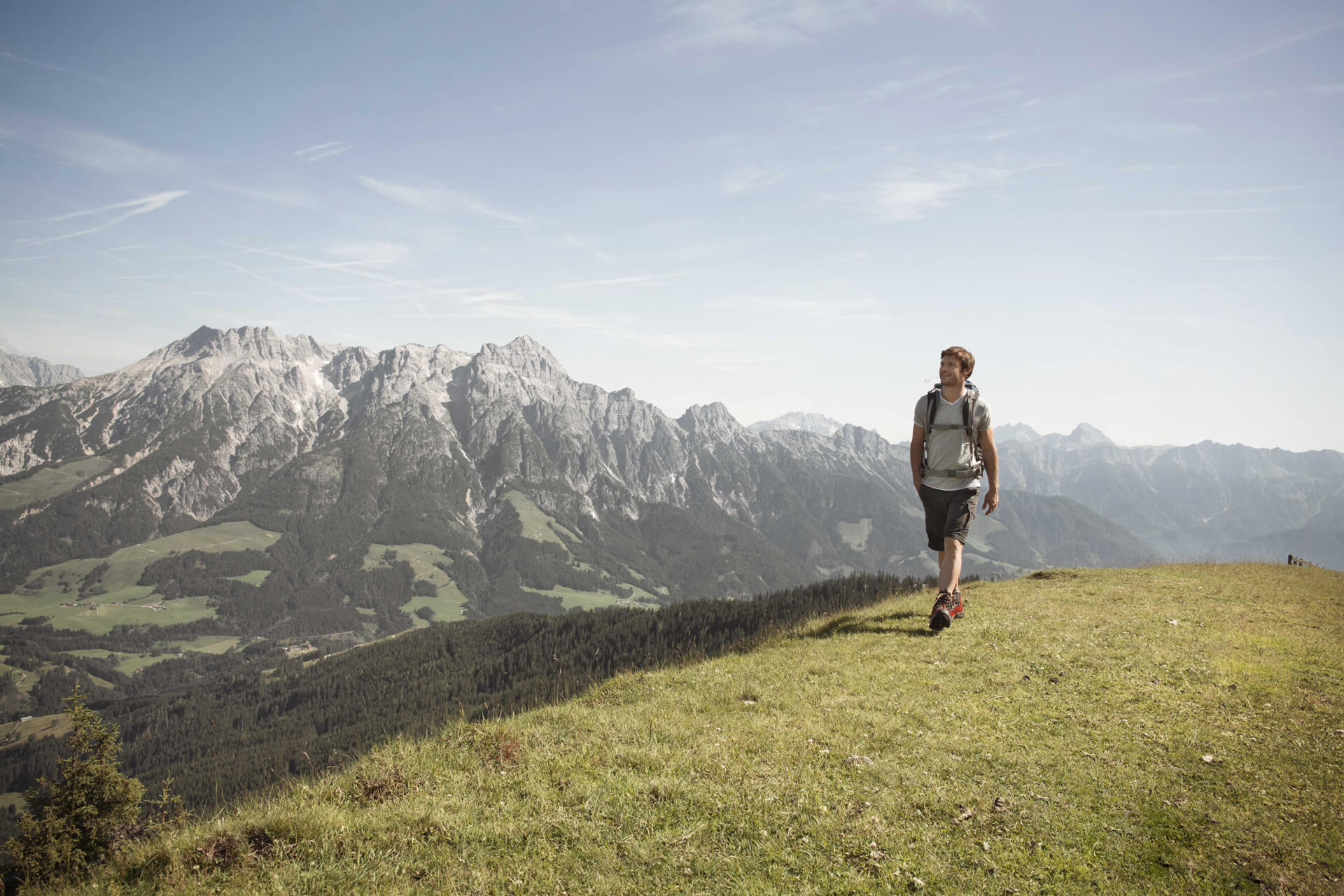 Mann beim Wandern über eine Almwiese, im Hintergrund schroffe Berge
