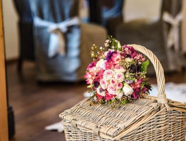 Ein Strauß rosa und weißer Blumen von bojoFARM ruht auf einem geflochtenen Weidenkorb in einem gemütlichen Innenbereich.