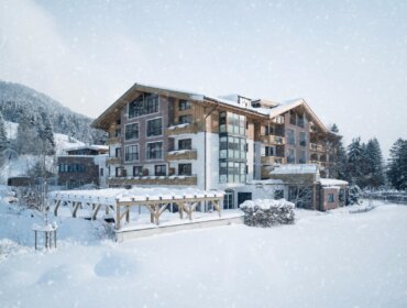 Ein großes Hotel im Chalet-Stil, umgeben von schneebedeckten Bäumen und Bergen, wenn es im Winter schneit.