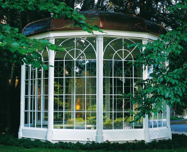 Gazebo in Hellbrunn, Sound of Music Ein weißer, verglaster Pavillon mit einem Kupferdach, der an den österreichischen Film Sound of Music erinnert, inmitten von üppigem Laub.
