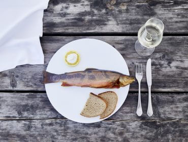 Ein ganzer gekochter Fisch, Zitrone, Roggenbrot und Weißwein auf einem rustikalen Holztisch.