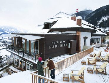haus_hirt_winter Zwei Personen gehen vor dem schneebedeckten Hotel & Spa Haus Hirt spazieren, im Hintergrund sind die Berge zu sehen.