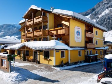Schneebedecktes Hotel Egger - gelbe Fassade mit Holzbalkonen